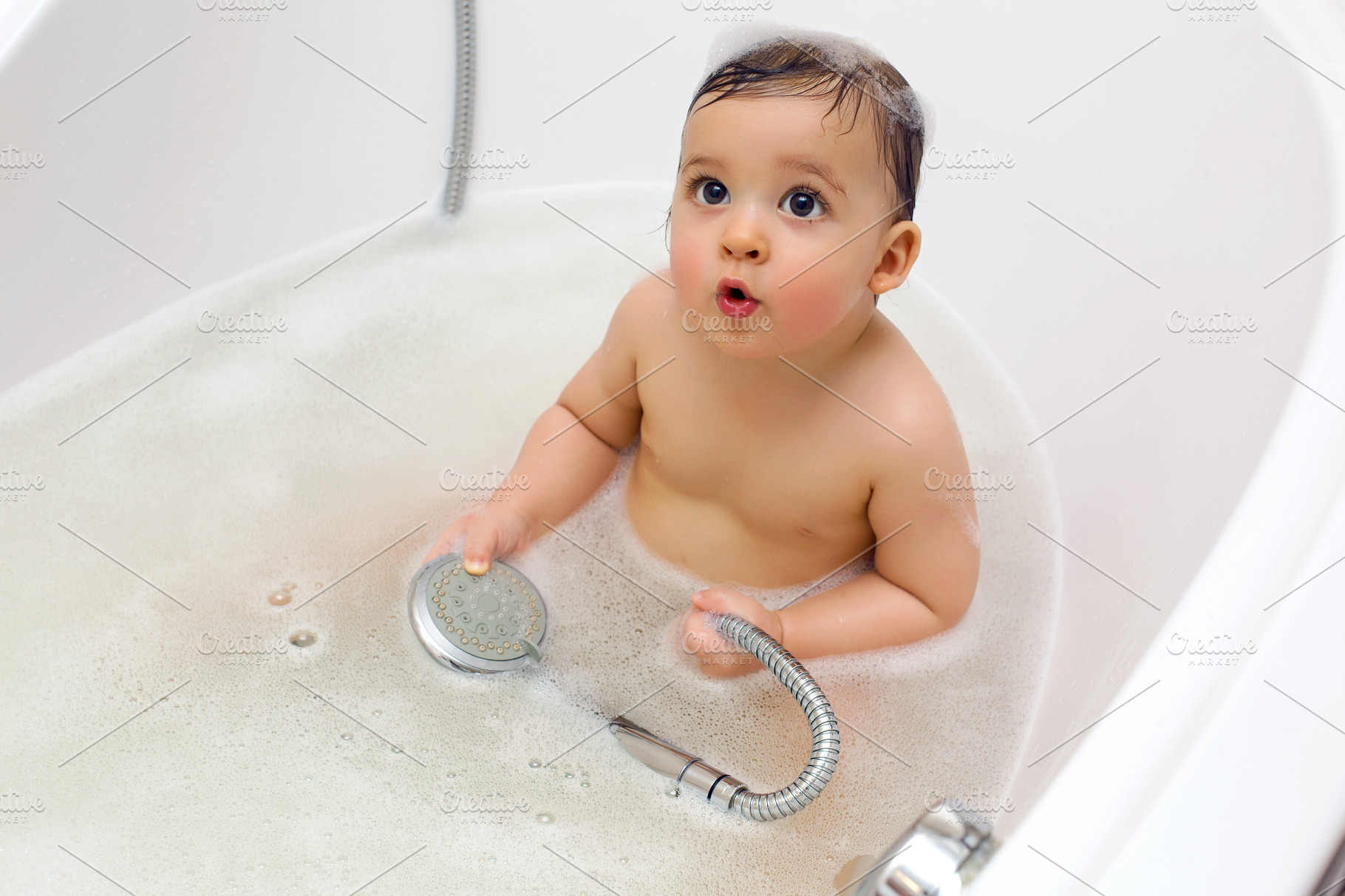 Baby boy sitting in bath with water featuring bath, bathroom, and